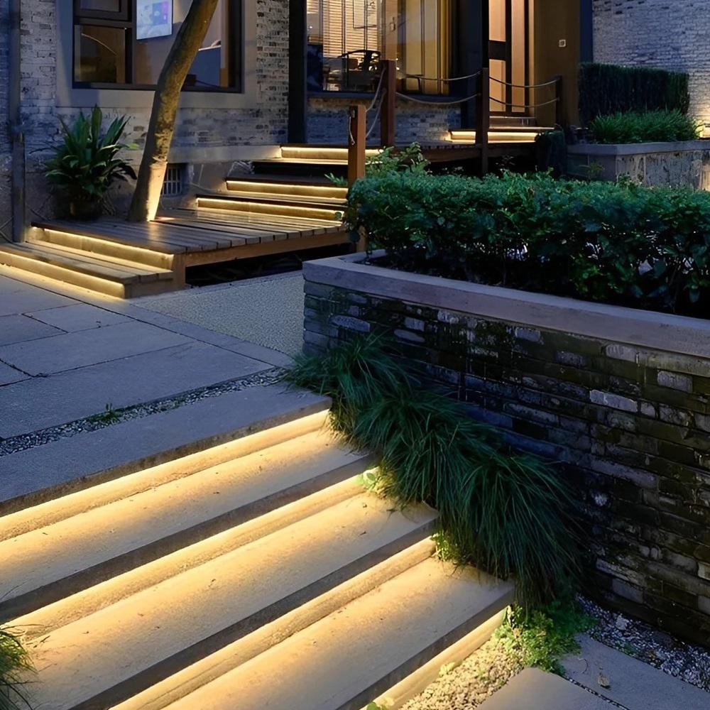 Outdoor steps and wooden deck illuminated with warm white COB LED strip lighting integrated into stair edges and garden landscape for ambient night lighting